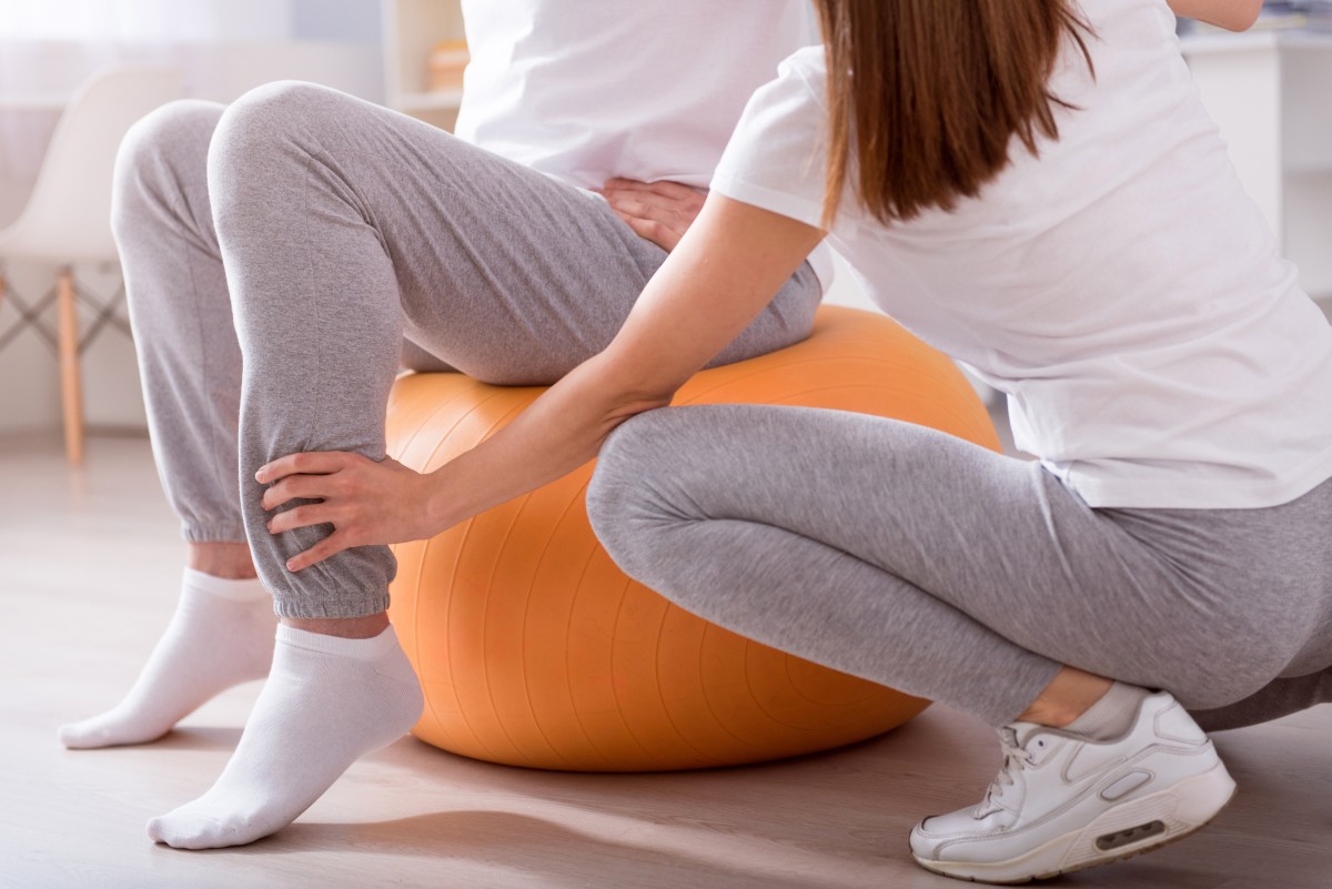 Healthy. Cropped picture of male patient sitting on gym ball with female physiotherapist performing some rehab exercises