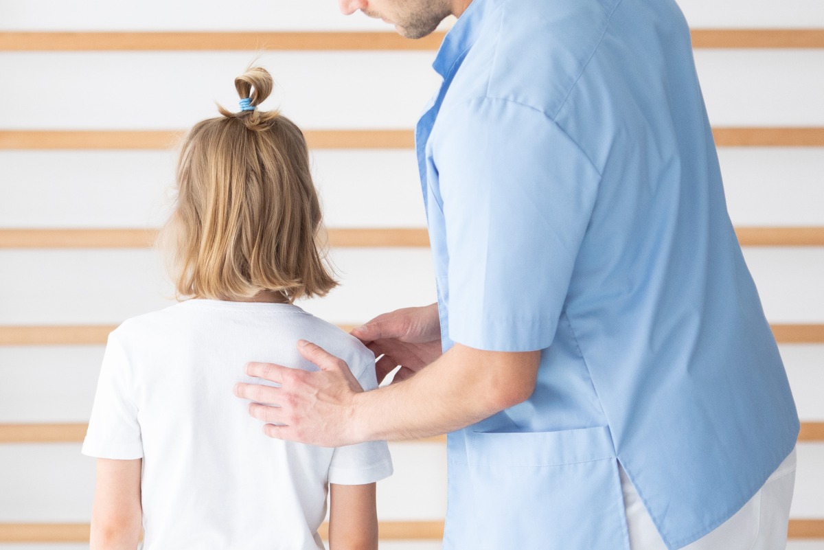 Male physiotherapist examining girl with scoliosis during rehabilitation